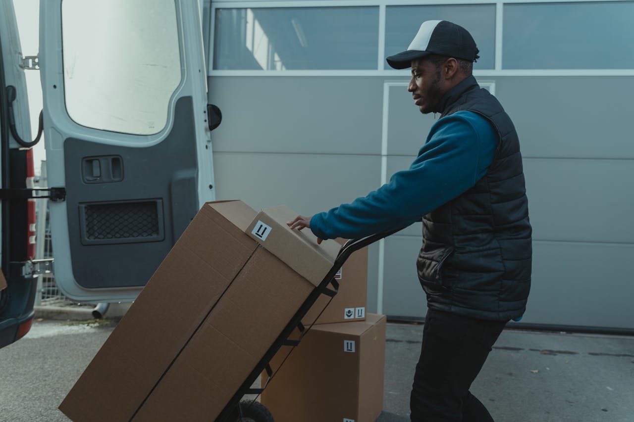 A courier delivers cardboard boxes using a trolley outdoors.